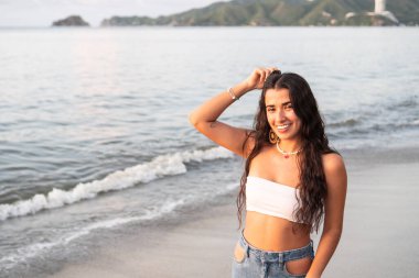 Genç bir kadın sahilde güneşli bir günün tadını çıkarırken okyanusta dikiliyor.