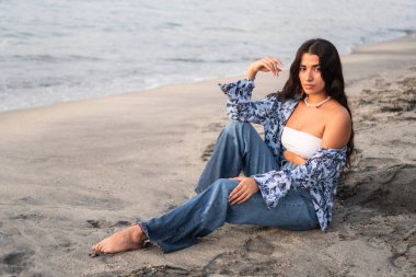 Kumsalın kıyısında kumsalda oturan kadın.