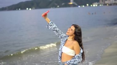 Genç kadın sahilde dans ediyor. Gün batımında uzun saçlı bir kız dans ediyor.. 