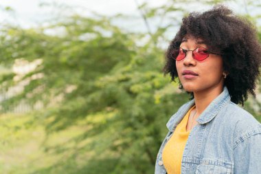 Ciddi bir kadın, yeşil arka planda dikilirken kameraya bakıyor.