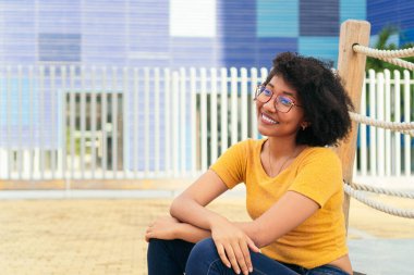 Genç bir kadın, günlük giysiler içinde, parkın merdivenlerinde oturuyor..