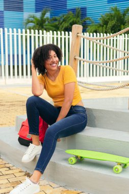 Normal giyinmiş, parkın merdivenlerinde oturan etnik kökenli pozitif bir kadın..