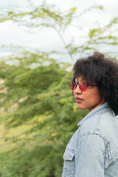 stock image Afro woman looking back to camera while standing outside over a natural green background