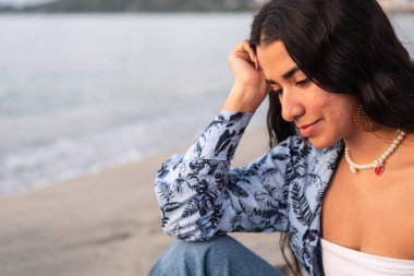 Genç bir kadın gün batımında sahilde takılıyor.