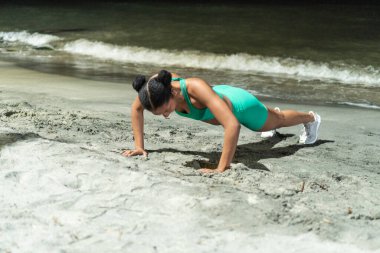 Plajda şınav çeken siyah bir sporcu.