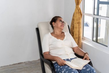 Latin kadın oturma odasında otururken kitap okumaktan zevk alıyor..