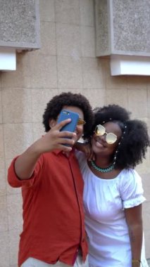 Afro saçlı bir çift şehirde selfie çekiyor.