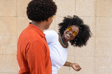 ethnic couple looking at each other against a brick wall.