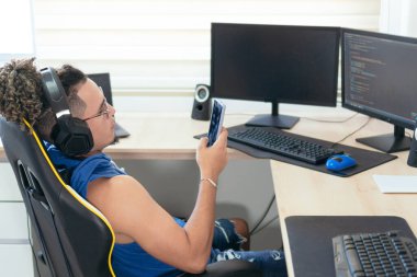 Computer programmer sitting in his office and typing on his cell phone.