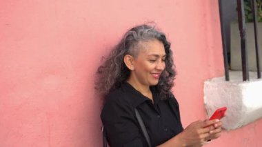 Older woman celebrating while looking at her cell phone in the street