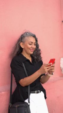 Latin woman celebrating while looking at her cell phone in the street