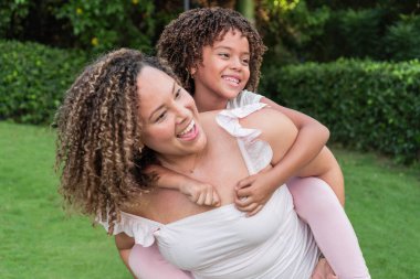 Curly-haired mother having fun with her daughter in the park