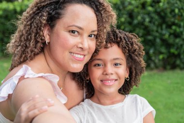 Happy mother and daughter smiling and hugging in a park.