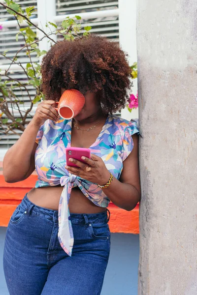 Afro Woman checking cell phone during coffee break