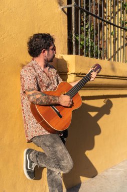 Genç adam gün batımında şehir sokaklarında gitar çalıyor.