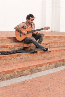 Sokak müzisyeni kaldırımda oturmuş para karşılığı gitar çalıyor.