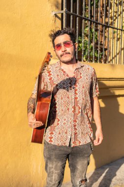 Latin müzisyen elinde gitarıyla sokakta dikiliyor.