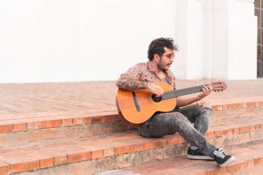 Sokak müzisyeni sokakta bir merdivende gitar çalıyor.