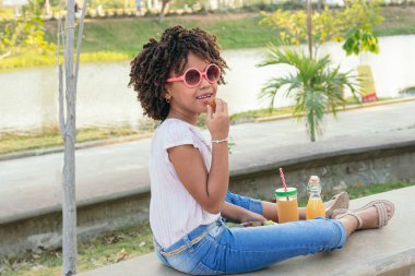 Parkta otururken sebze yiyen kız.