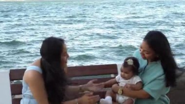 Anne bebeğini kucağında tutuyor ve bir arkadaşıyla konuşuyor.