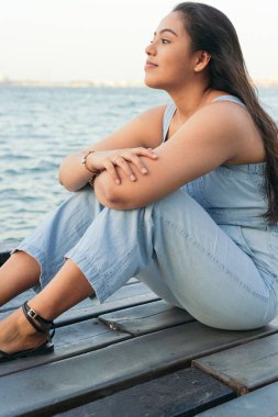 Latin kadın bir iskelede oturuyor, bir yaz gününde dalgın..