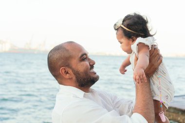 Neşeli Baba, bebeğini gökyüzünde büyütür ve ona gülümser.