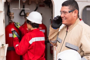 Mühendis telefonda konuşuyor, iş arkadaşıyla endüstriyel arkaplanda çalışıyor.
