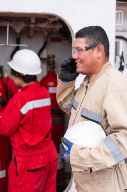 Latin Mühendis telefonda konuşuyor, iş arkadaşıyla endüstriyel arkaplanda çalışıyor.