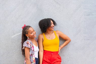 Gri bir duvarın önünde duran iki arkadaş