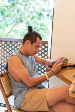 Latin bir adam masada oturmuş cep telefonunu kontrol ediyor.