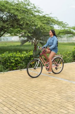 Genç bir kadın güneşli bir parkta bisiklet sürüyor..