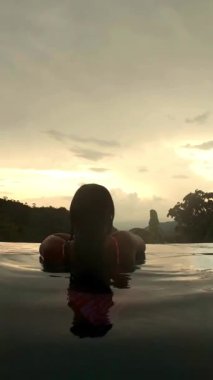 Havuzda sırtüstü dağlara bakan Latin kadın.