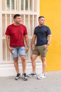 Yaz kıyafetleri içinde iki adam şehir sokaklarında yürürken sohbet ediyorlar.
