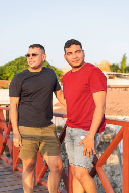 İki adam gün batımının tadını çıkarıyor, köprü korkuluklarına yaslanmış.