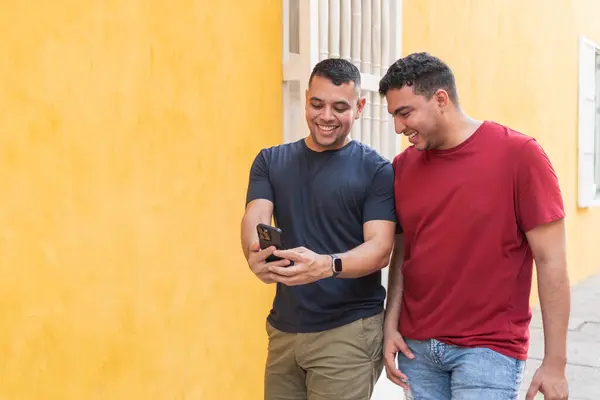 Two men share a laugh while looking at a smartphone together.