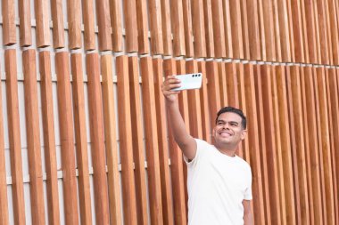 Diş teli takmış neşeli genç bir adam ahşap arka planda selfie çekiyor..