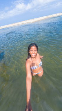 Güneşli gökyüzünün altında berrak deniz sularında yürüyen bikinili gülümseyen kadın..