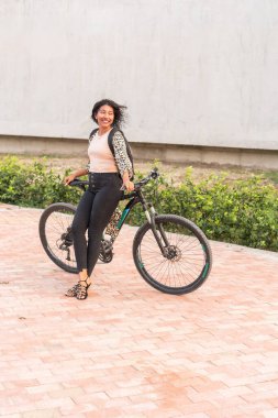 Şehir ortamında bisikletle yürüyen gülümseyen bir kadın.
