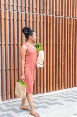 Yazlık elbiseli genç bir kadın elinde taze yeşillikler, düşünceli görünüyor..
