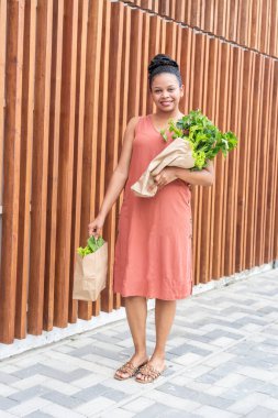 Elinde bir çanta dolusu yeşillik ve poşet tutan neşeli genç bayan..