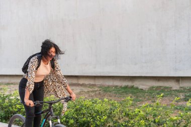 Leopar desenli hırkalı genç bir kadın bisikletini şehir yolunda itiyor..