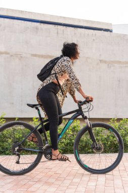Bisikletine binmeye hazır, leopar desenli bluzu ve siyah kotu olan bir kadının yan görüntüsü..