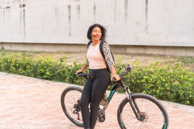 Parlak gülüşlü genç bir kadın bisikletiyle poz veriyor, şık bir leopar desenli hırka giyiyor..