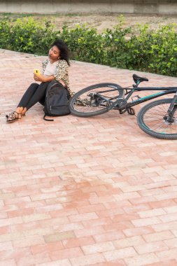 Ringa kemiğinden yapılma bir yolda uzanan bir kadın yanında bisikletiyle telefonunu kullanıyor..