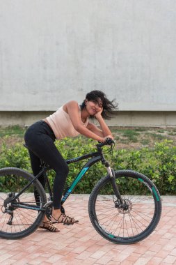 Yorgun genç bir kadın mola sırasında alnından ter silerken bisikletinin üzerinde dinleniyor..