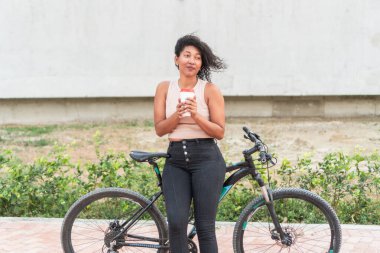 Bisikletinin yanında duran bir kadın bir fincan kahvenin tadını çıkarıyor, açık havayı soluyor..