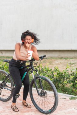 Bir kadın neşeli bir anı paylaşır, elinde kahveyle kıkırdar, bisikletine yaslanır..