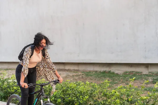 Leopar desenli hırkalı genç bir kadın bisikletini şehir yolunda itiyor..