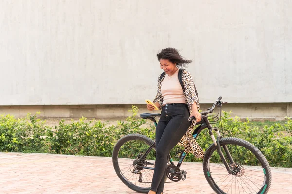 Genç bir kadın bisikletinin yanında leopar desenli ceketi olan akıllı telefonunu kontrol ediyor..