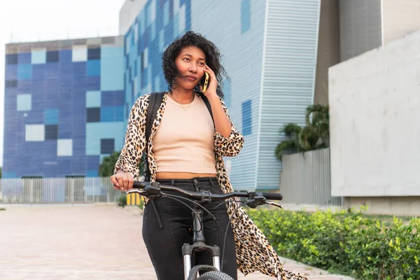 Leopar desenli hırkalı profesyonel bir kadın bisikletle yürürken telefonla konuşuyor..